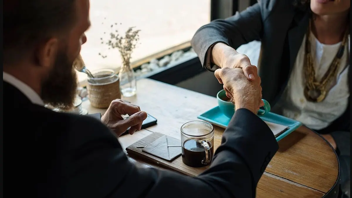 Two people shaking hands across a café table