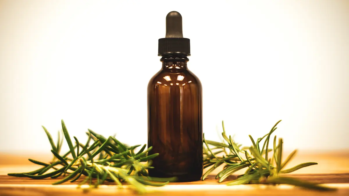 A bottle of rosemary oil beside fresh rosemary