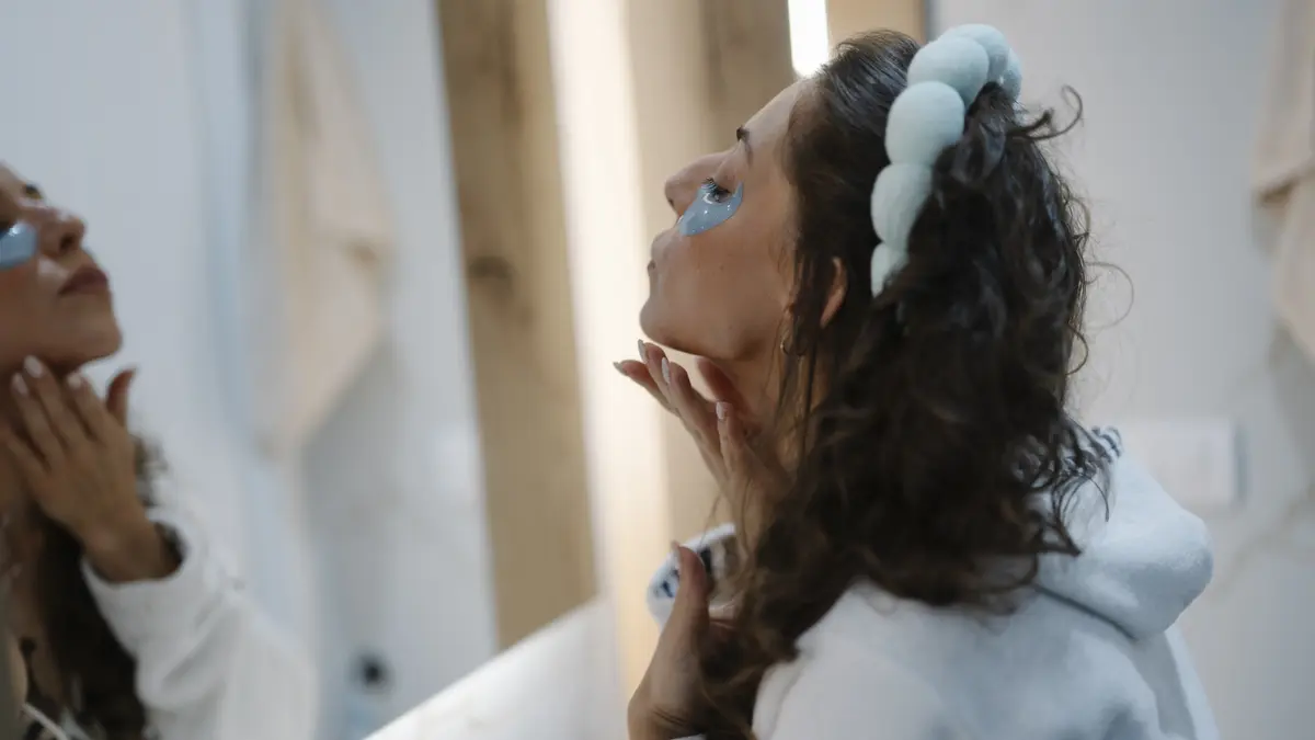 A woman applying a skincare product in a bathroom mirror