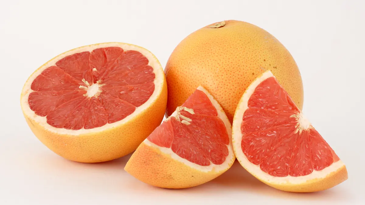 Whole and sliced pink grapefruit on a light background