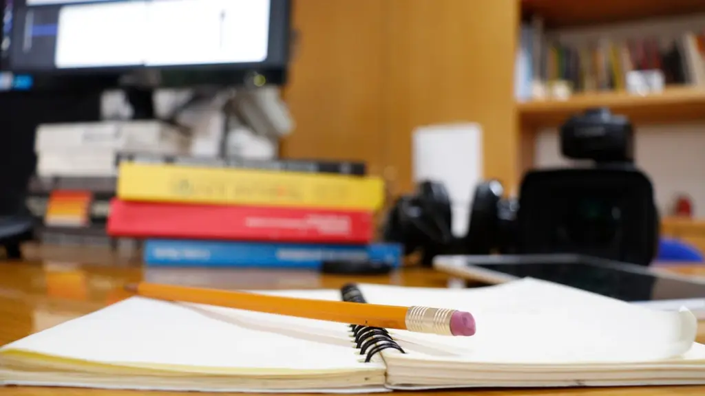 An open notebook and pencil on a desk beside books